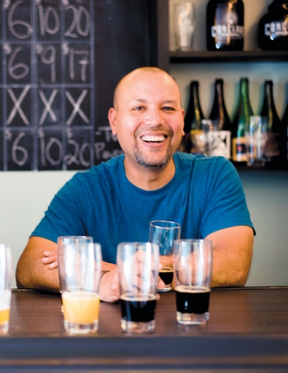 Carl Alfaro, co-owner of Conclave Brewery, smiling behind a selection of beers set up to taste.